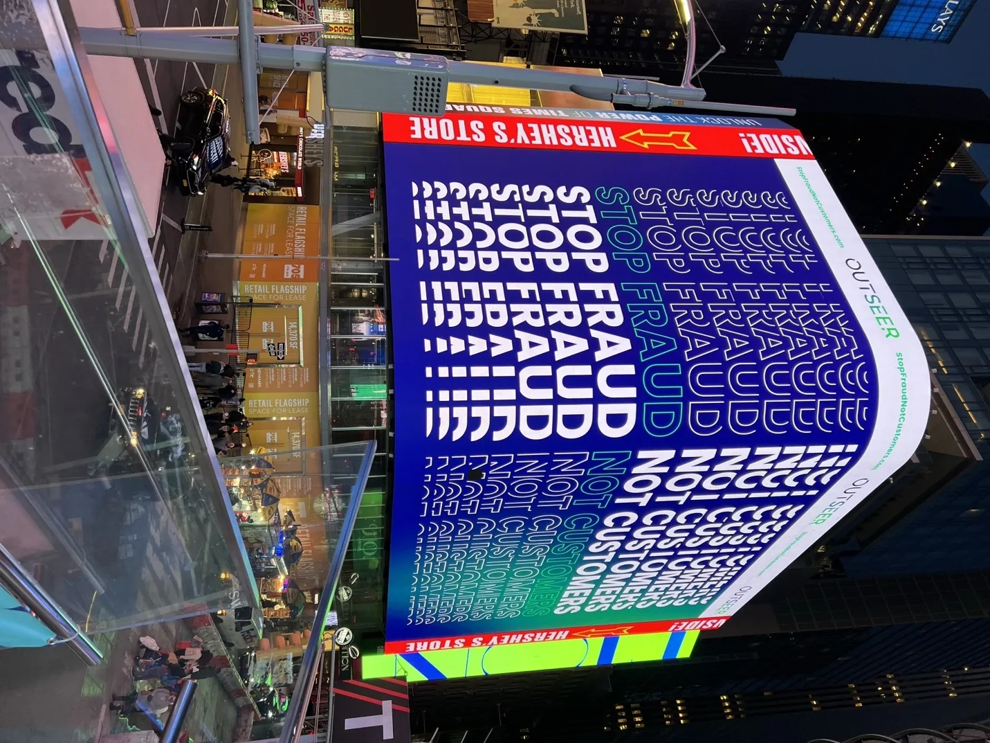 The Stop Fraud Not Customers campaign running on a large curved billboard in Times Square at night.